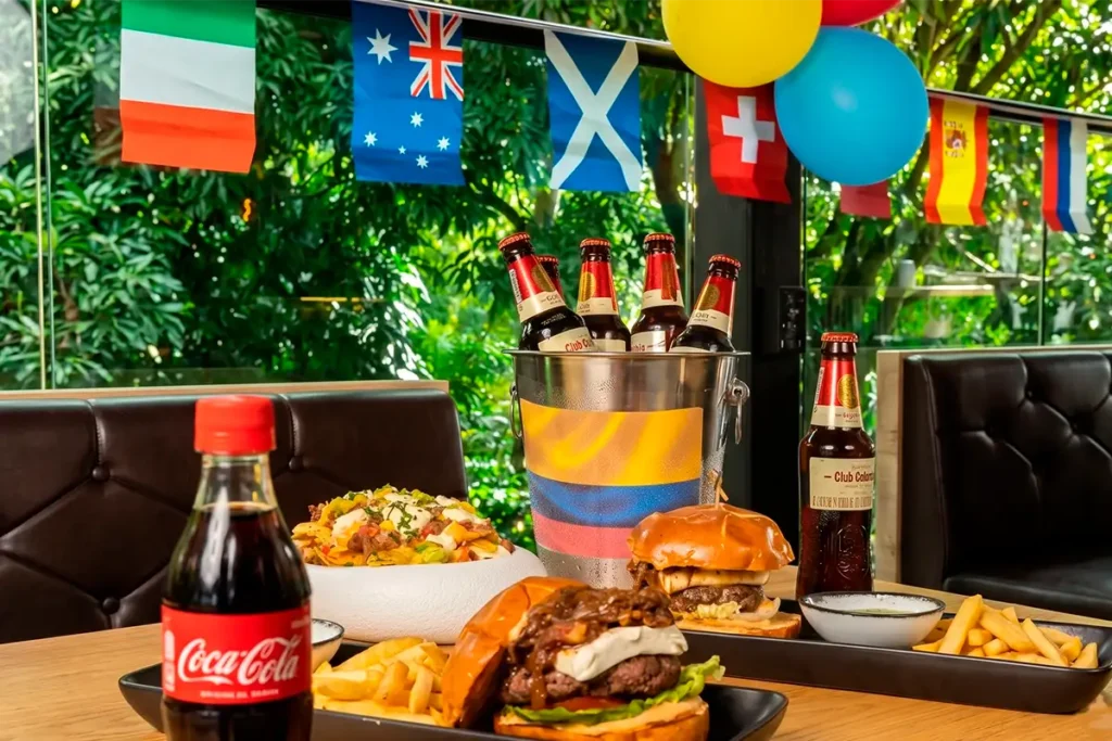 Mesa con hamburguesas, cervezas y banderas del mundo en Café Hotel Medellín.